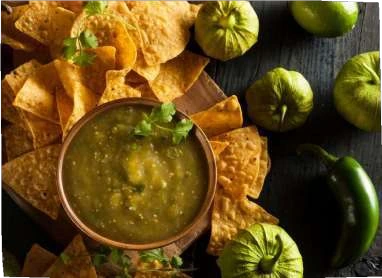 Salsa Verde in a bowl surrounded by tortilla chips and green ingredients.